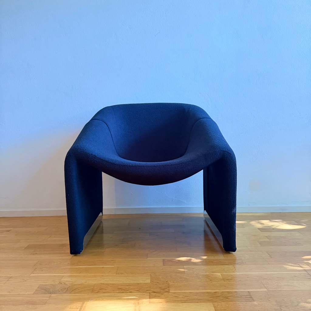 A modern sculptural armchair upholstered in black fabric, set against a light blue wall on a light wood floor.