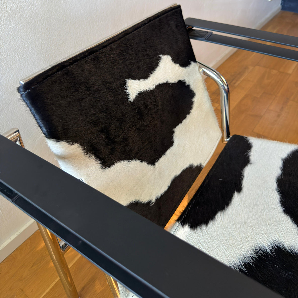 A modern chair with a black and white cowhide seat and backrest, featuring a black metal frame and a light wood floor in the background.