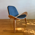 A modern wooden lounge chair with a curved natural wood frame and dark blue upholstered seat and back, placed on a light wood floor against a plain wall.